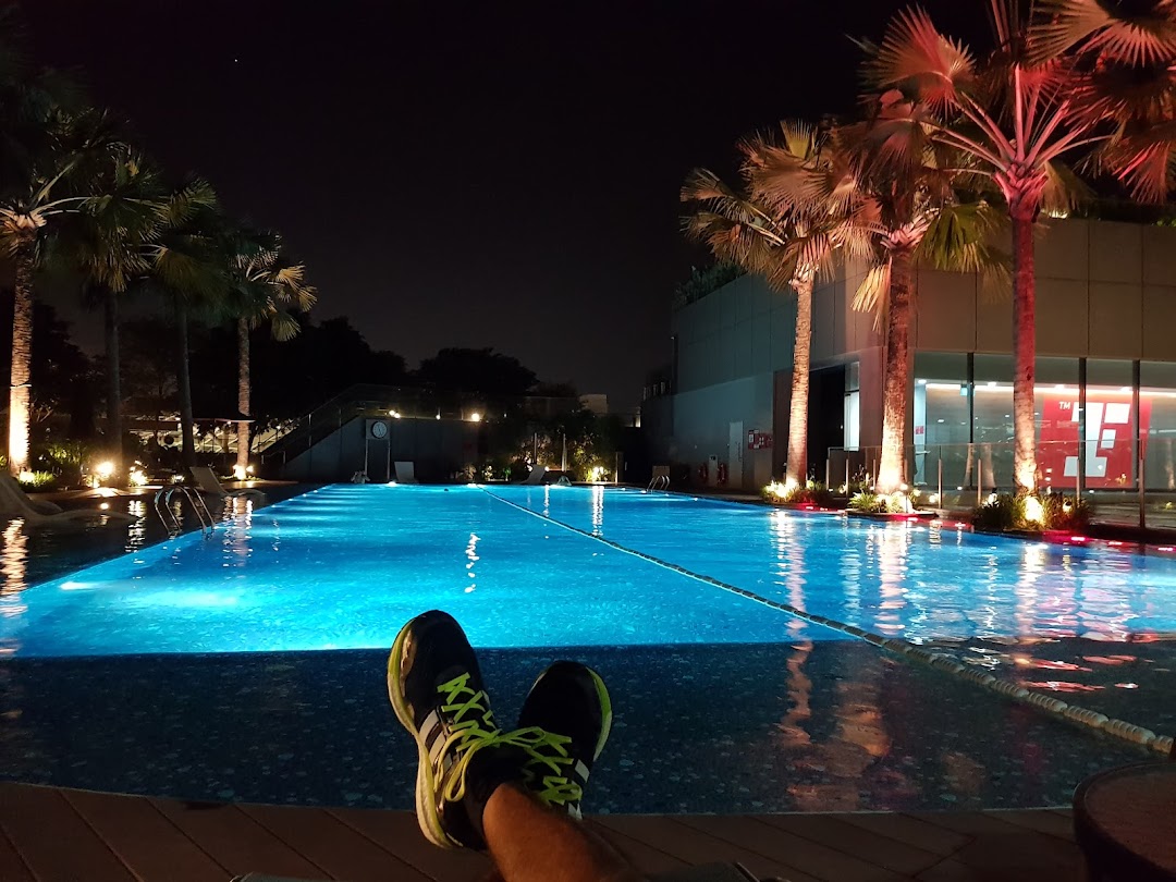 A person's feet resting by a beautifully lit swimming pool at night, surrounded by palm trees.