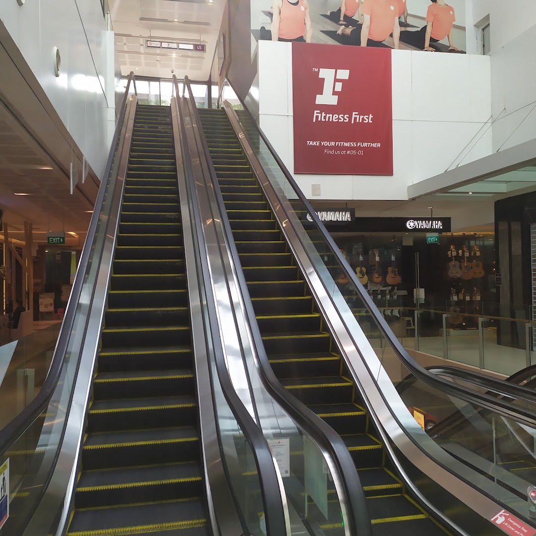 Escalators leading up to a Fitness First advertisement banner in a shopping mall.
