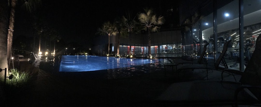 A beautifully lit swimming pool at night with a modern gym visible through glass windows in the background.
