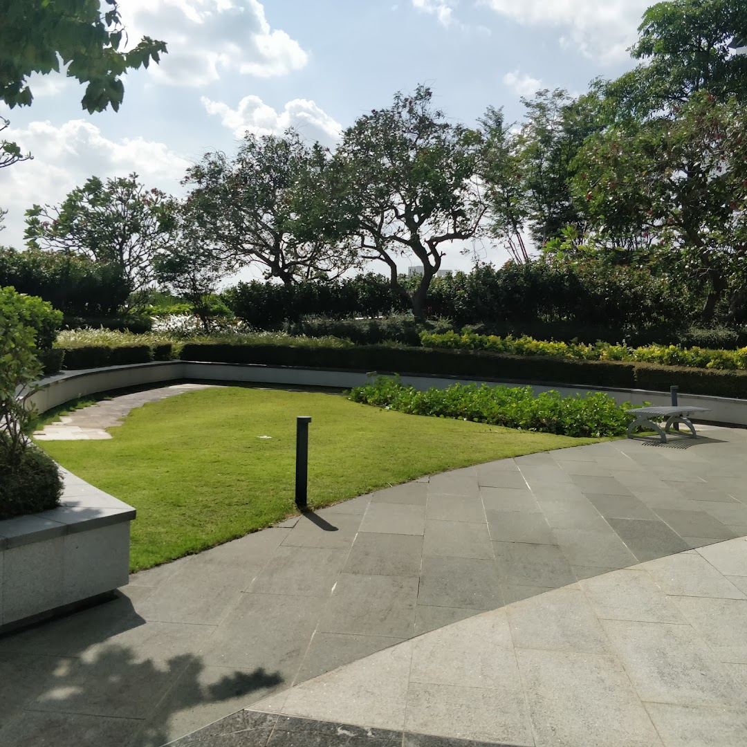 A serene outdoor garden area with lush green grass, paved pathways, and mature trees under a bright sky.