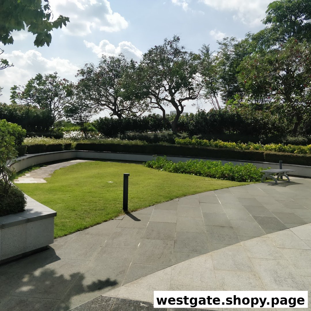 A serene outdoor garden area with lush green grass, paved pathways, and mature trees under a bright sky.