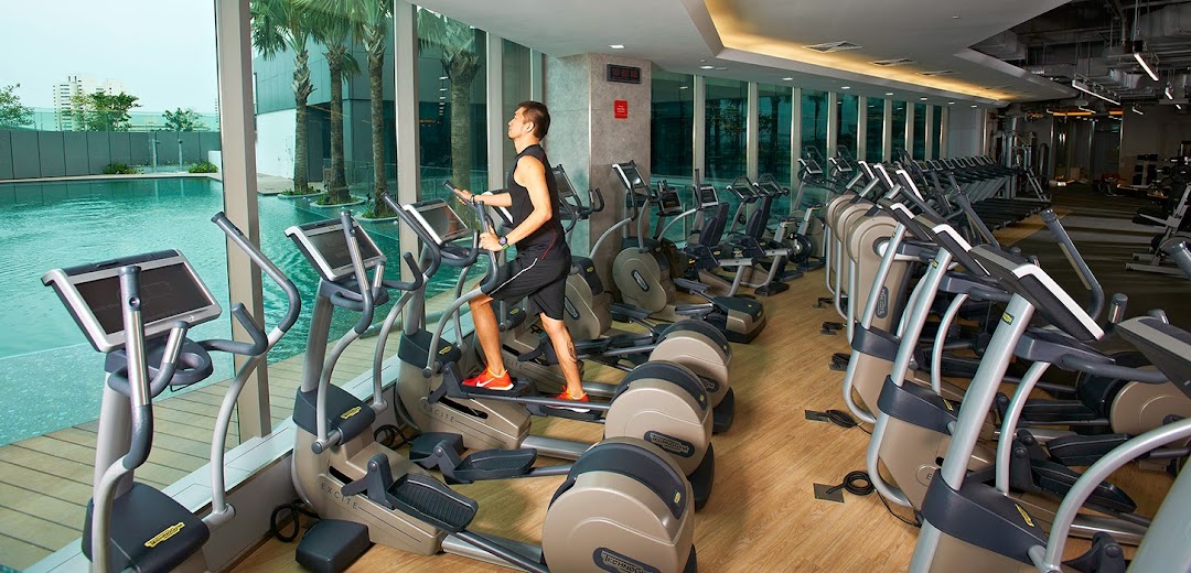 A person exercising on an elliptical machine in a modern gym with large windows overlooking a pool.