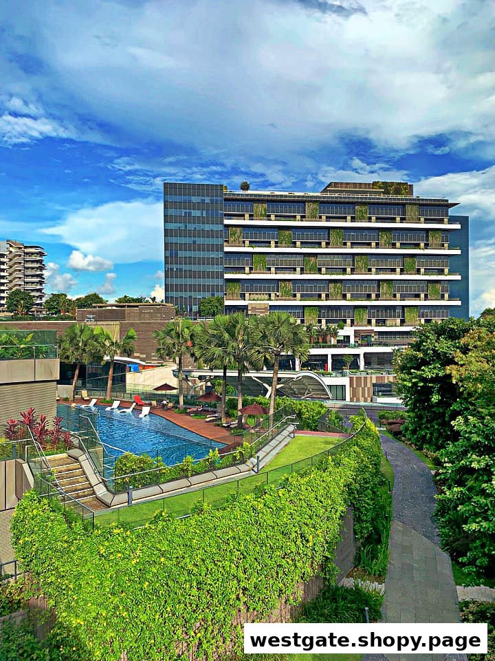 An aerial view of a modern building with a swimming pool and lush green landscaping under a blue sky.