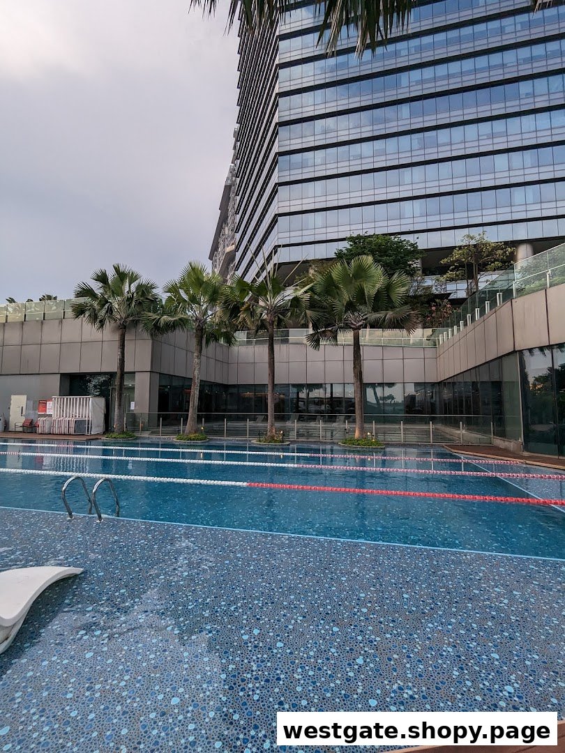 An outdoor swimming pool with lane markers and palm trees, set against a modern building.