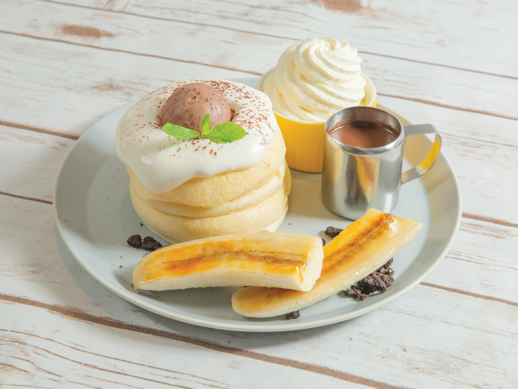 A plate of fluffy soufflé pancakes topped with cream, chocolate ice cream, and caramelized bananas.