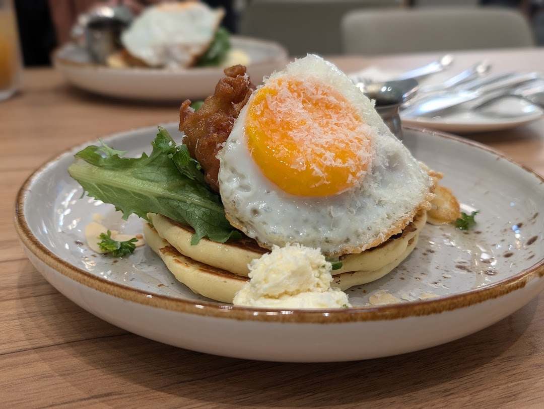 A close-up of a delicious dish featuring pancakes, a fried egg, fried chicken, and greens.