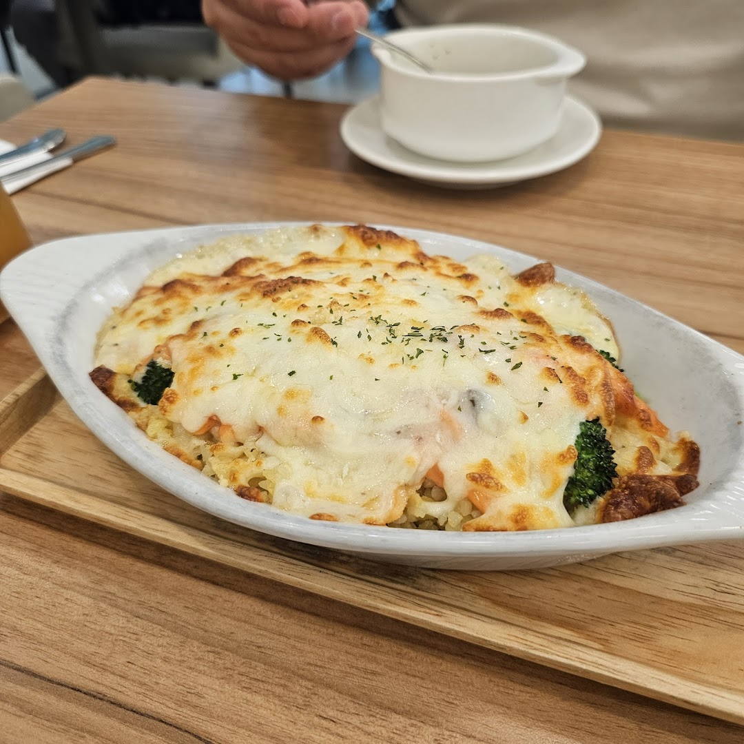 A close-up of a delicious baked dish with melted cheese, salmon, and broccoli served on a wooden tray.
