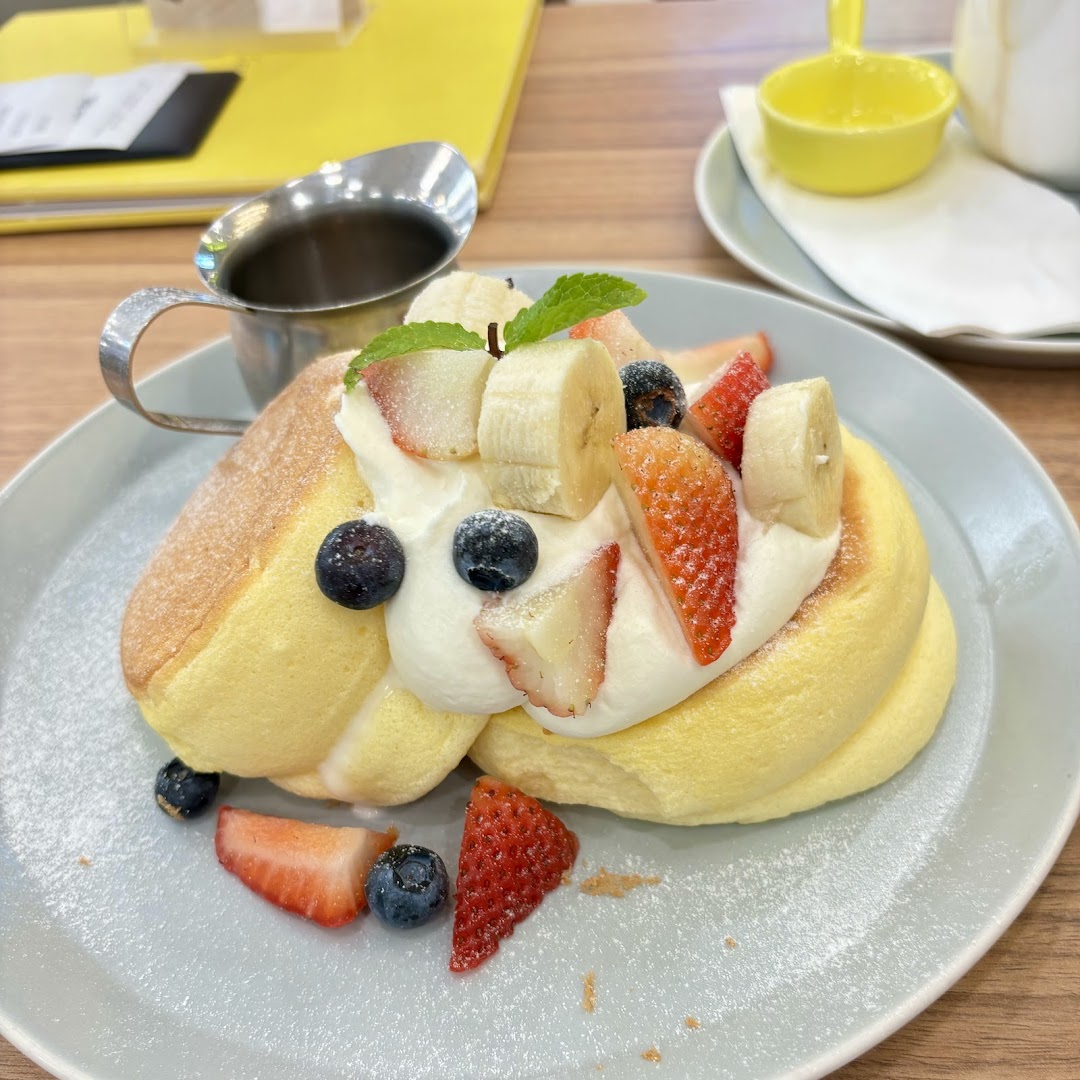 Fluffy soufflé pancakes with fresh berries, banana, whipped cream, and powdered sugar.