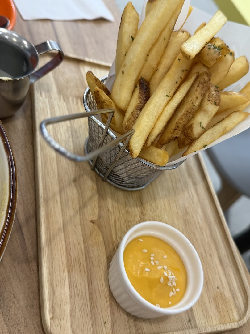 A serving of golden fries in a metal basket with a side of creamy dip on a wooden tray.