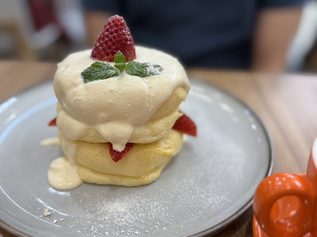 A stack of fluffy soufflé pancakes topped with cream, strawberries, and mint on a grey plate.