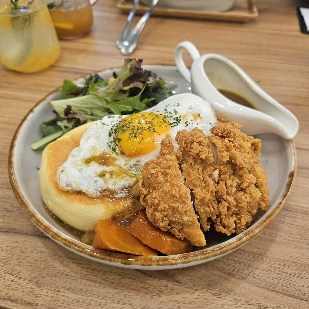 A delicious plate featuring crispy fried chicken, a fluffy pancake, fried egg, and curry sauce with vegetables.