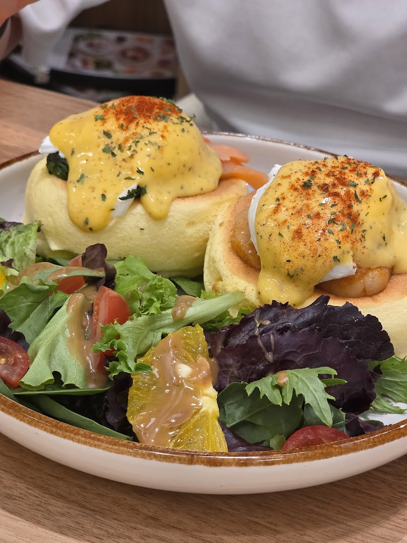 A plate of fluffy soufflé pancakes topped with hollandaise sauce, poached eggs, and a fresh side salad.