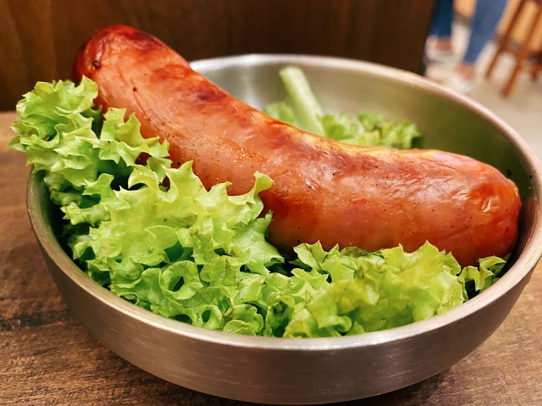 A close-up of a grilled sausage served on a bed of fresh green lettuce in a metal bowl.
