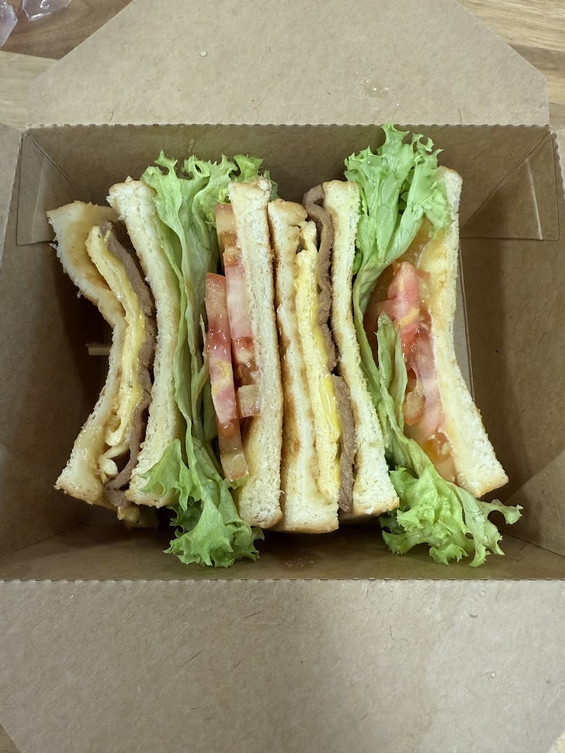 A delicious sandwich with fresh lettuce, tomato, and fillings, presented in a takeaway box.