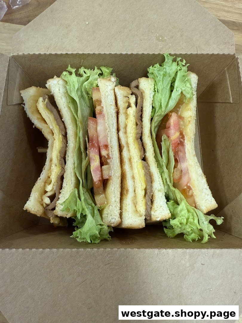 A delicious sandwich with fresh lettuce, tomato, and fillings, presented in a takeaway box.