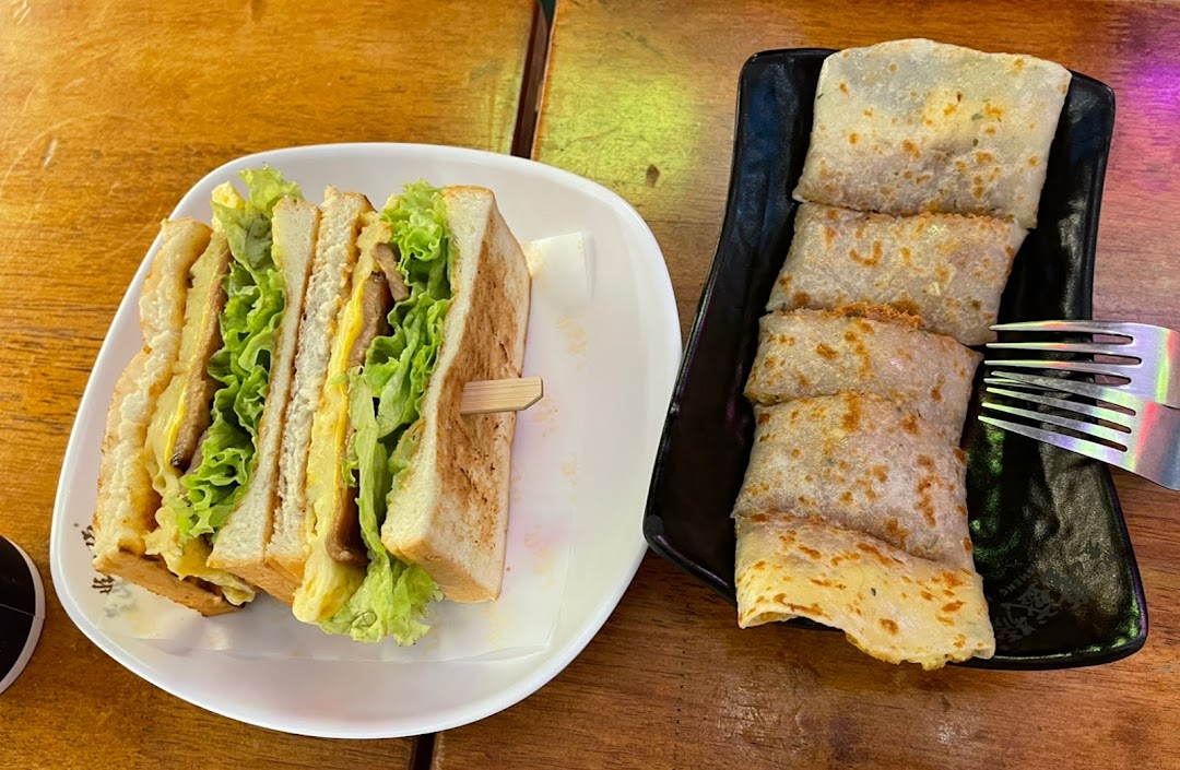 A delicious club sandwich and savory Taiwanese egg crepes on a wooden table.