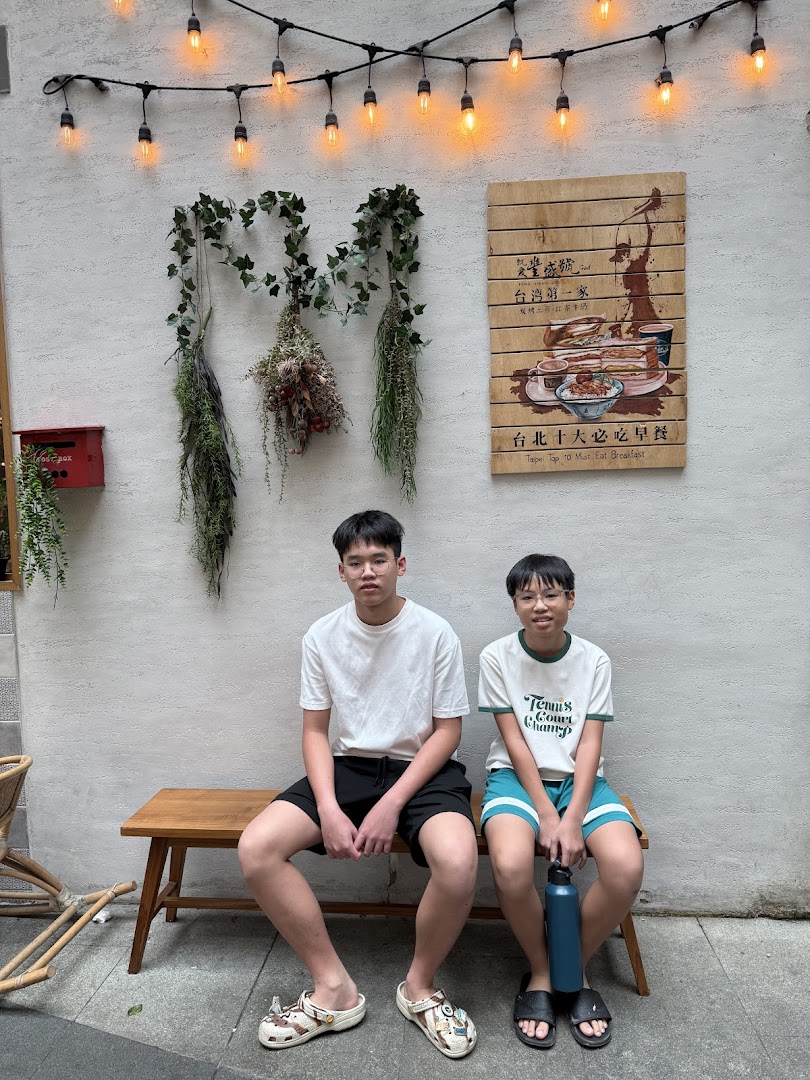 Two individuals relaxing on a wooden bench outside Fong Sheng Hao, featuring decorative lighting and a breakfast sign.