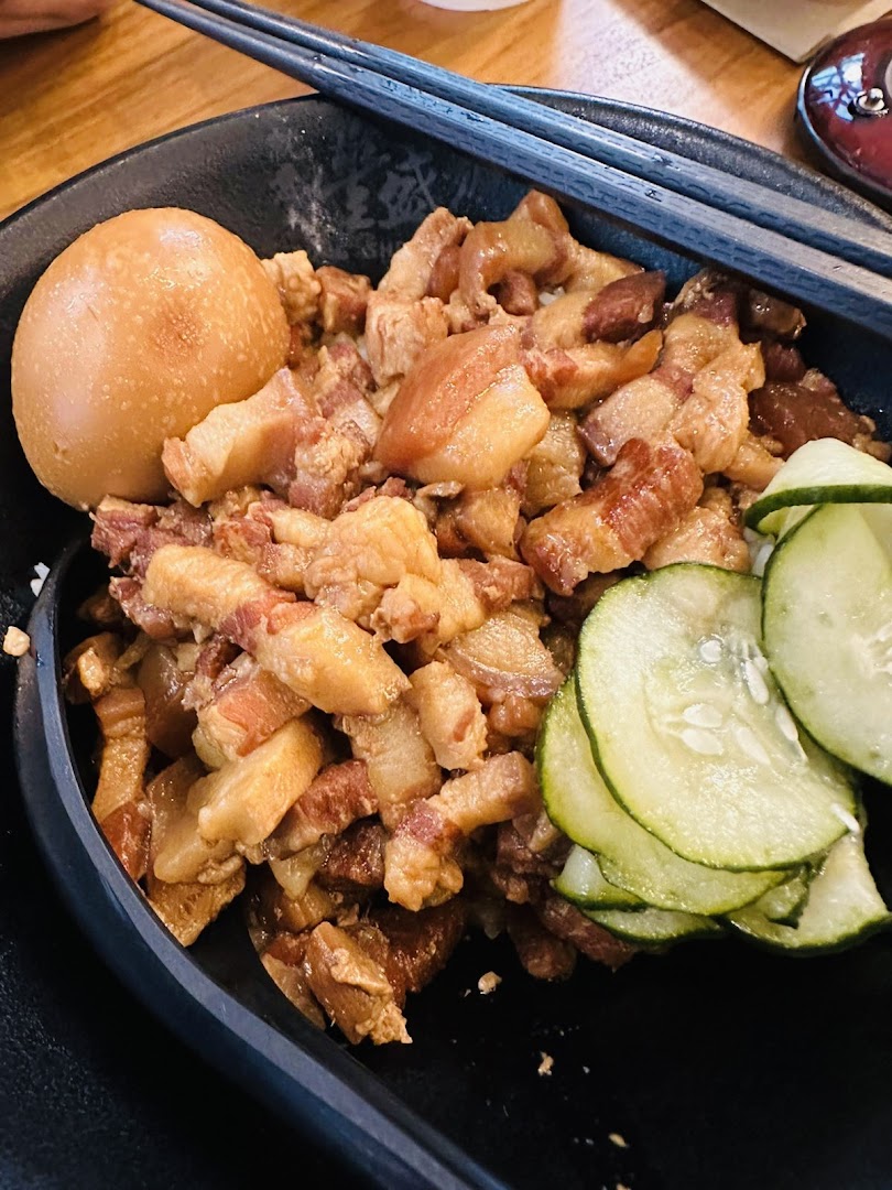 A close-up of a delicious bowl of braised pork belly with egg and cucumber slices.