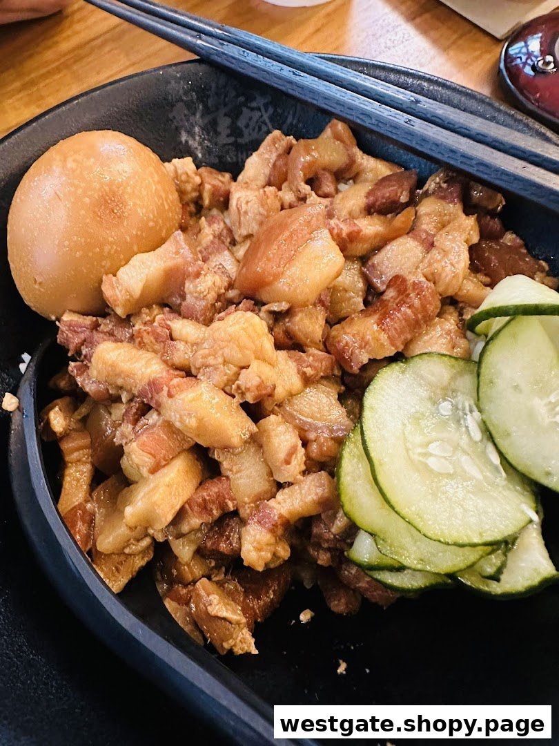 A close-up of a delicious bowl of braised pork belly with egg and cucumber slices.