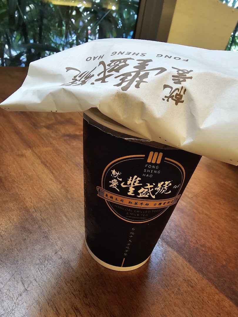 A branded drink cup and paper bag from Fong Sheng Hao on a wooden table.