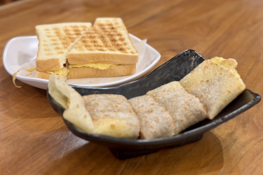 A toasted sandwich and a savory egg pancake roll served on a wooden table.