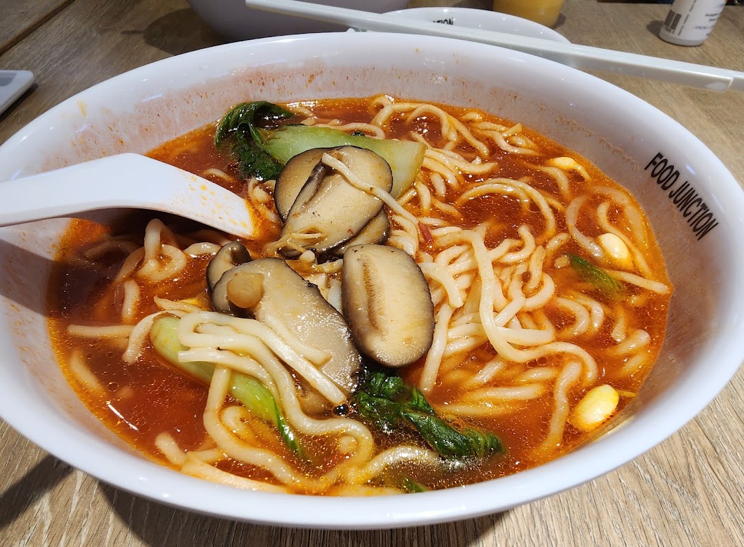A close-up of a delicious bowl of spicy noodles with mushrooms and greens from Food Junction.