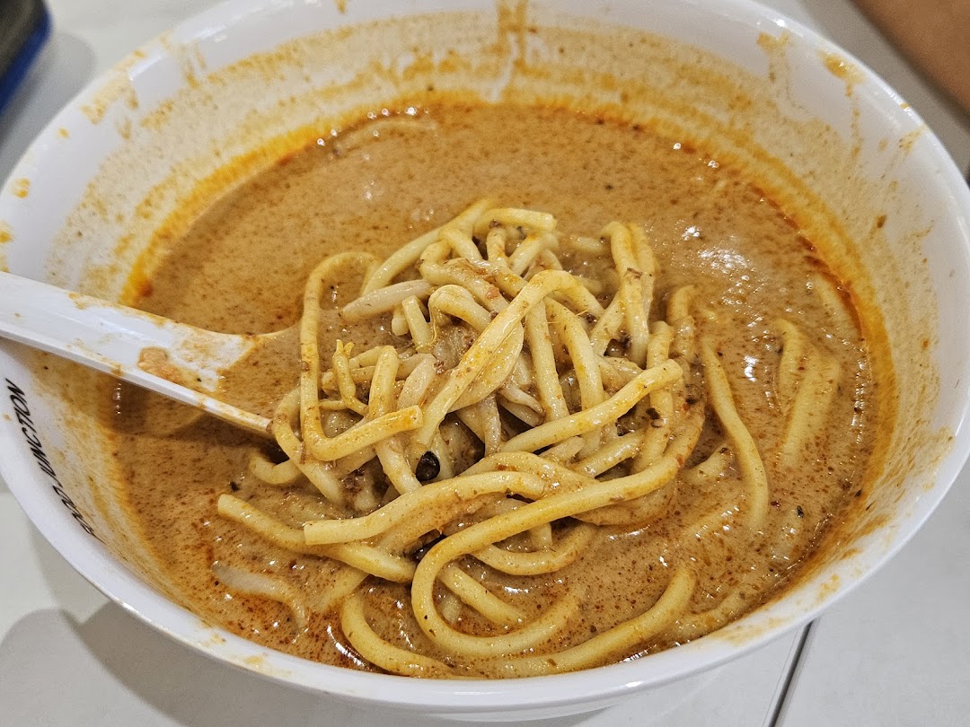 A close-up of a delicious bowl of curry noodles or laksa with a spoon.