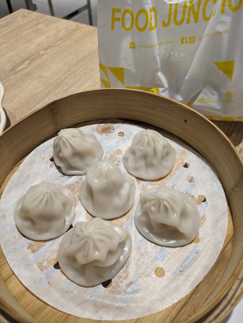 A bamboo steamer basket filled with freshly steamed dumplings, with a Food Junction bag in the background.