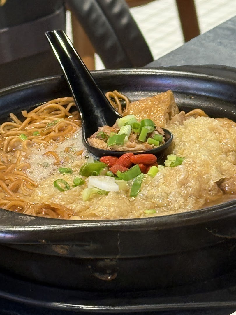 A close-up of a steaming bowl of noodles with various toppings and a spoon.