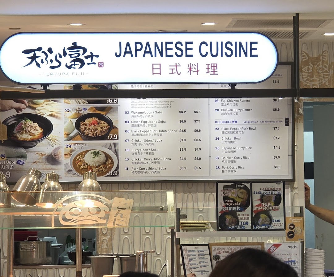 A Japanese cuisine stall's menu board displaying various udon, soba, ramen, and rice dishes.
