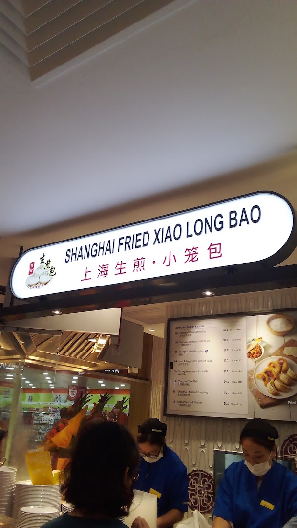 A food stall named 'Shanghai Fried Xiao Long Bao' with staff and a visible menu board.