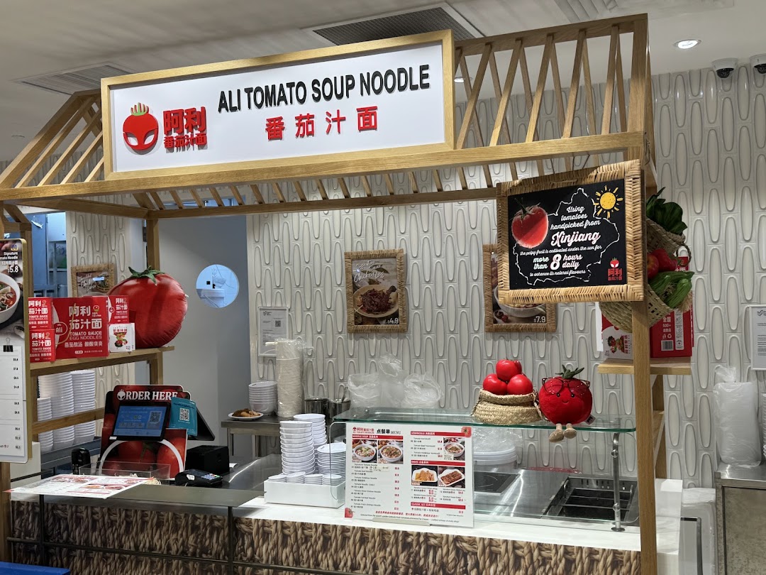 A vibrant food stall, Ali Tomato Soup Noodle, featuring a counter, signage, and tomato-themed decor.
