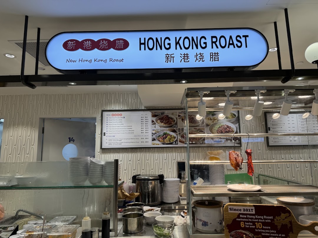 A food stall counter featuring a 'Hong Kong Roast' sign, menu boards, and hanging roasted meats.