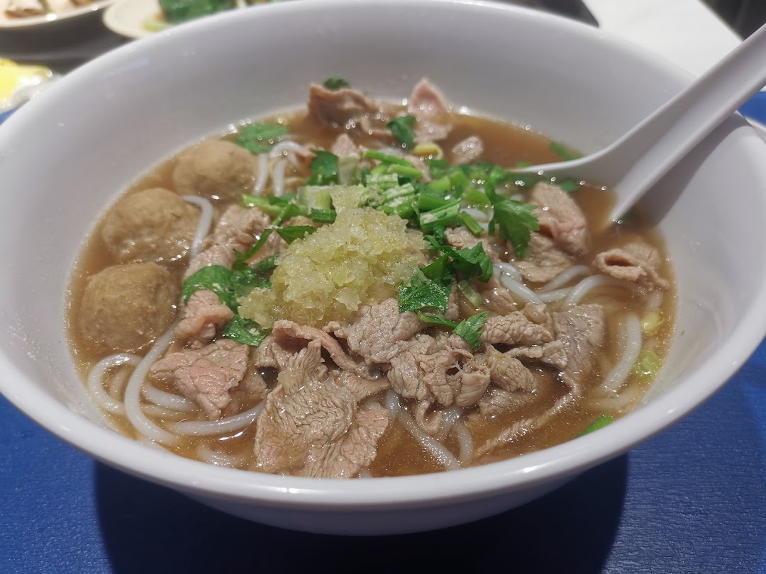 A close-up of a delicious bowl of beef noodles with meatballs and fresh herbs.