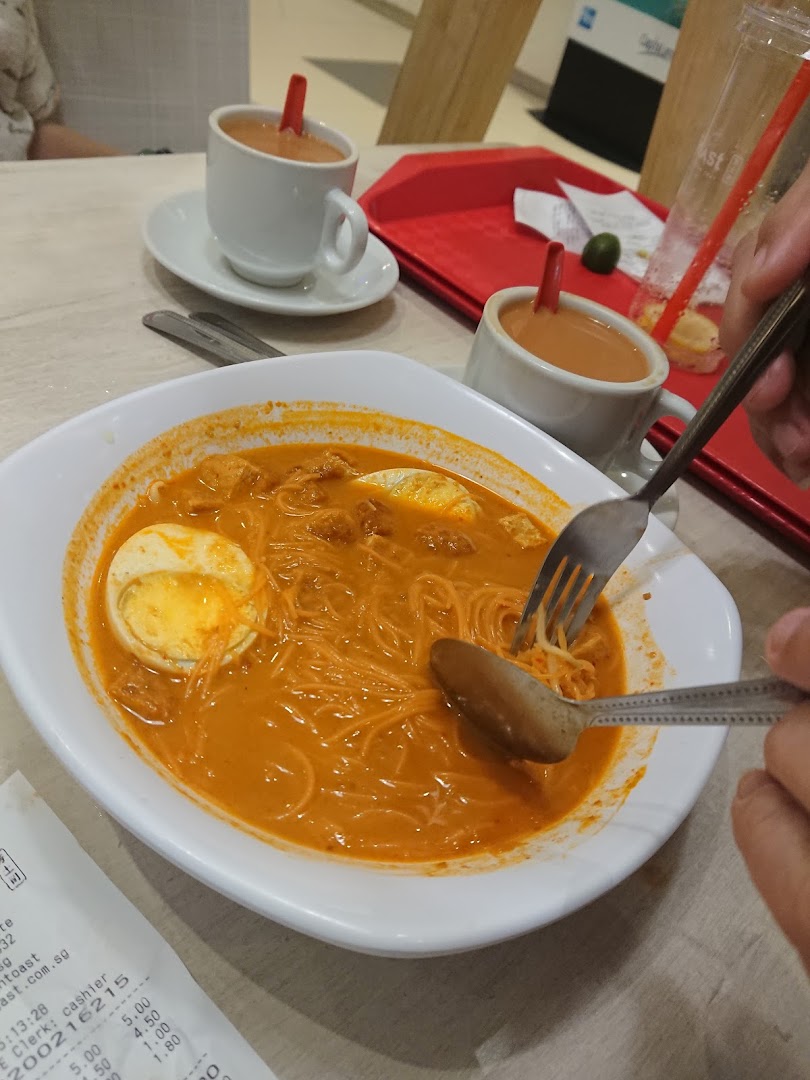 A bowl of curry noodles with egg and two cups of milk tea on a table at Fun Toast.
