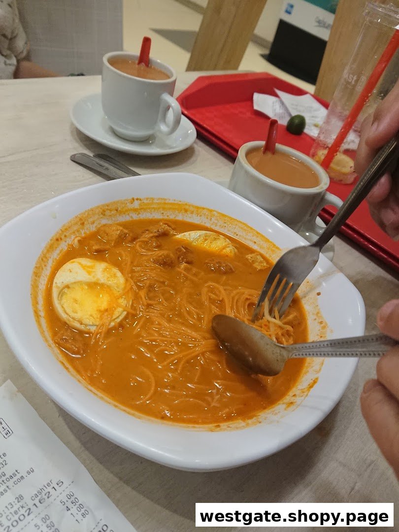 A bowl of curry noodles with egg and two cups of milk tea on a table at Fun Toast.