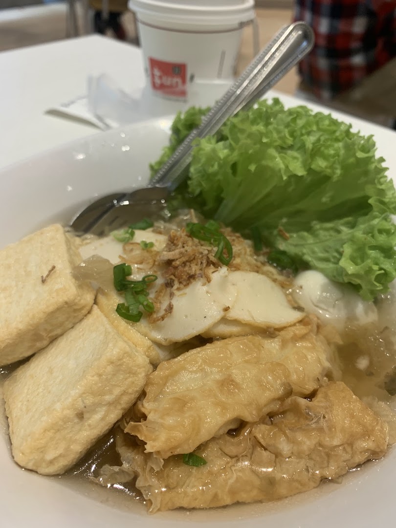 A close-up of a savory noodle dish with tofu, fish cakes, and fresh lettuce.