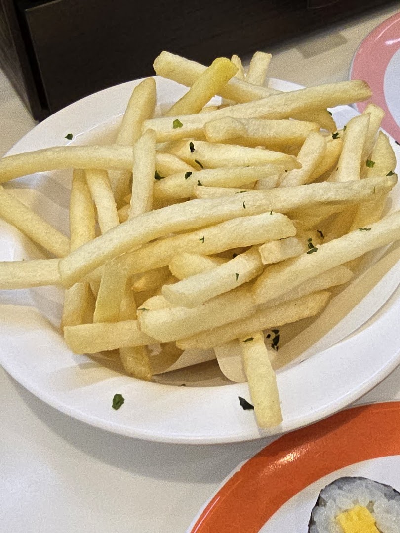A close-up of golden french fries sprinkled with herbs, served on a white plate.