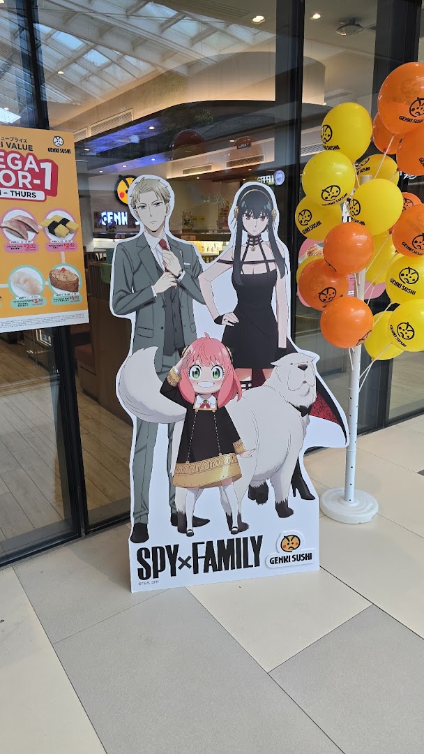 A promotional display at Genki Sushi featuring Spy x Family standees, balloons, and a special offer menu board.