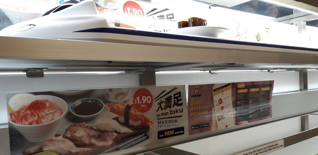 A sushi plate on a train delivery system at Genki Sushi, with promotional signs for membership and new items.