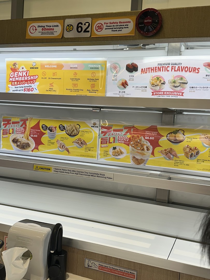 An interior view of Genki Sushi, showcasing its conveyor belt system, membership benefits, and various sushi and side dish promotions.