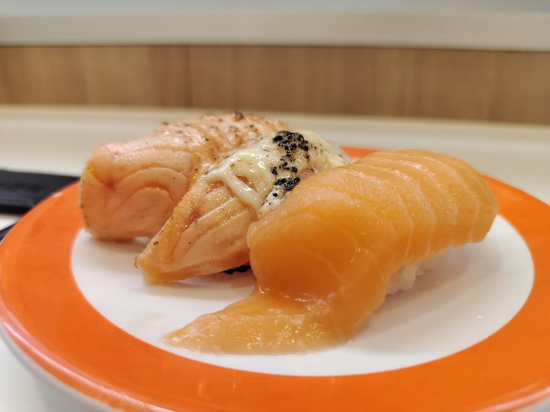 A plate of three salmon sushi pieces, including fresh and seared varieties, on an orange-rimmed plate.