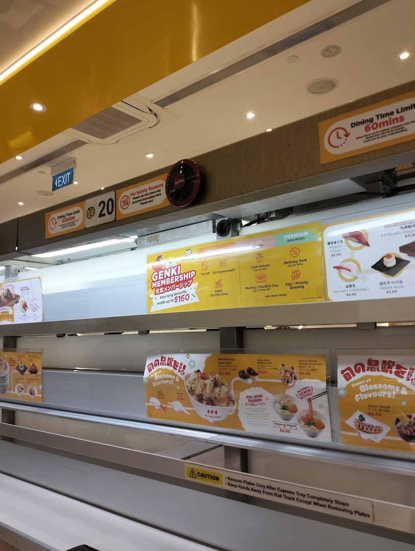 An interior view of Genki Sushi, showcasing its modern conveyor belt system and promotional displays.