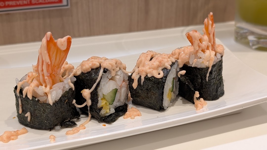 Close-up of delicious shrimp sushi rolls with creamy sauce on a white plate.