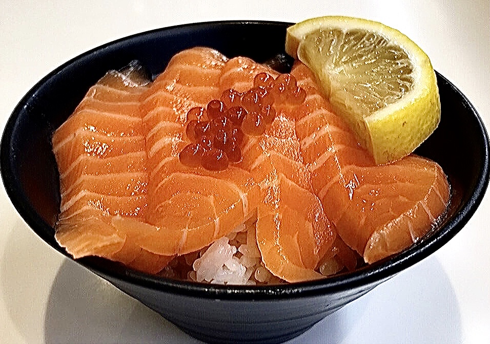A close-up of a vibrant salmon donburi bowl topped with ikura and a fresh lemon slice.