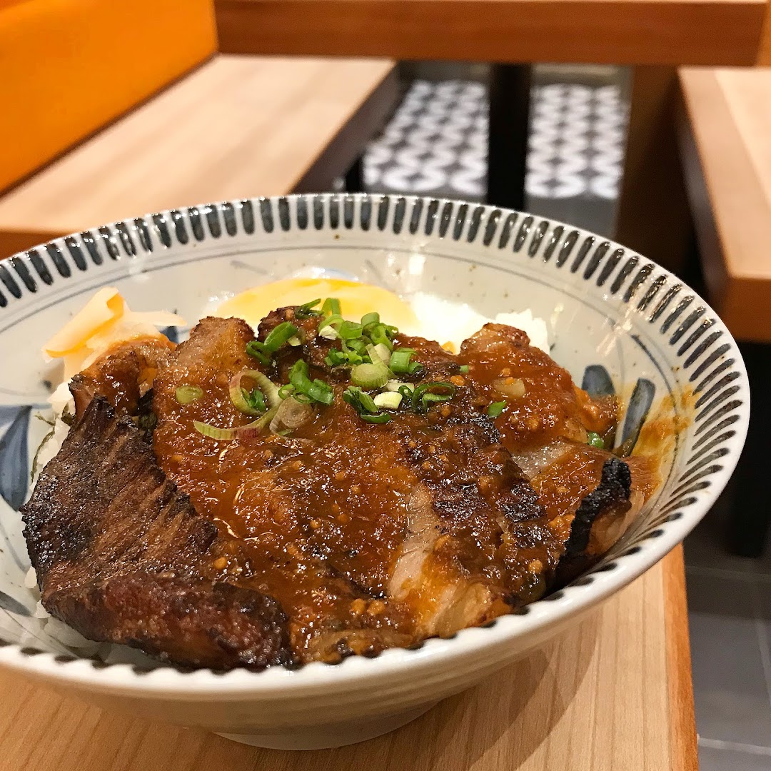 A close-up of a delicious Japanese rice bowl with grilled meat, sauce, and toppings.