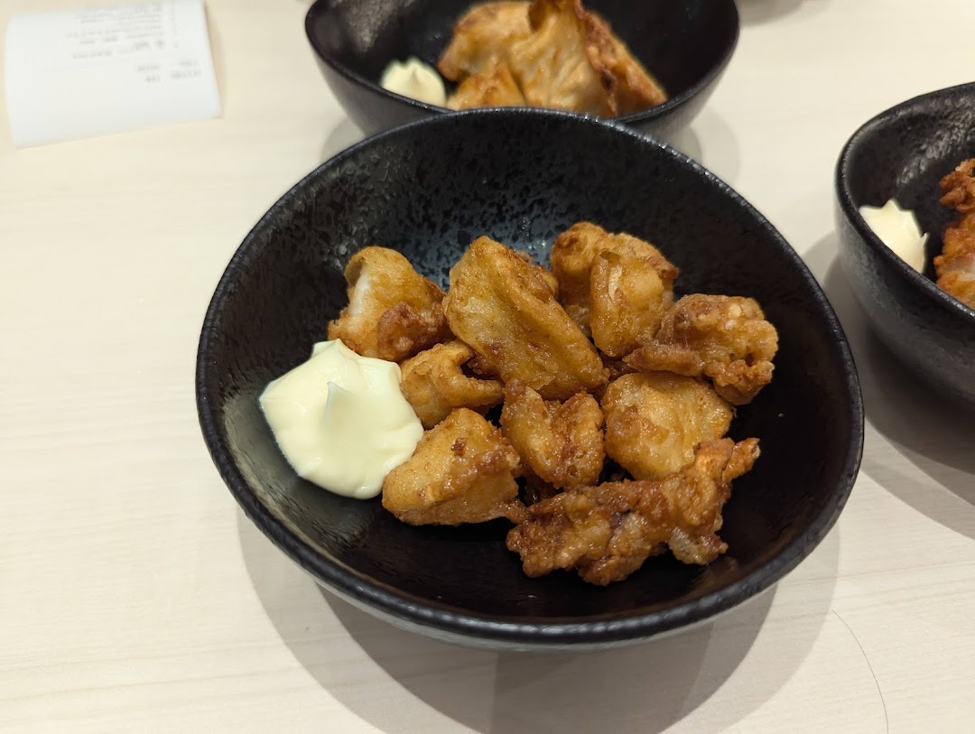 A black bowl filled with golden-brown fried chicken pieces and a dollop of mayonnaise.