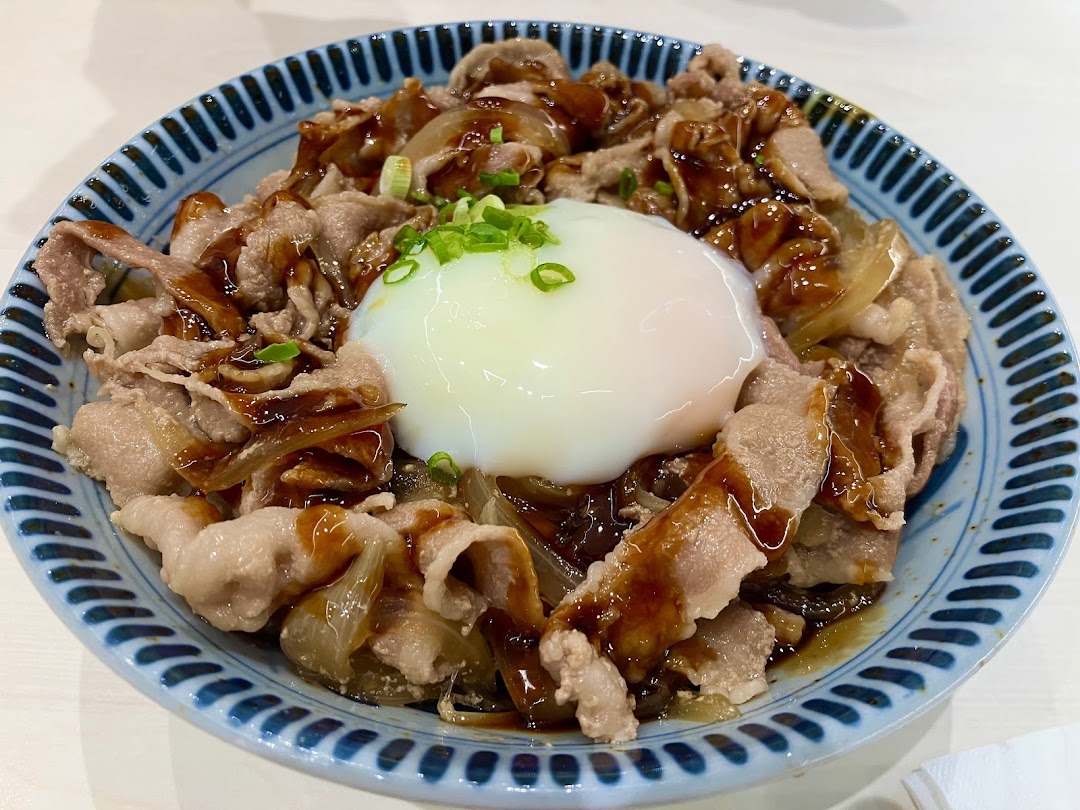A close-up of a Japanese rice bowl with tender sliced pork, sweet onions, and a creamy poached egg.