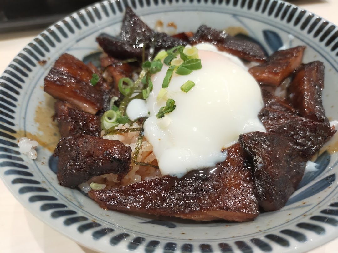 A close-up of a delicious Japanese rice bowl featuring tender braised meat and a perfectly poached egg.