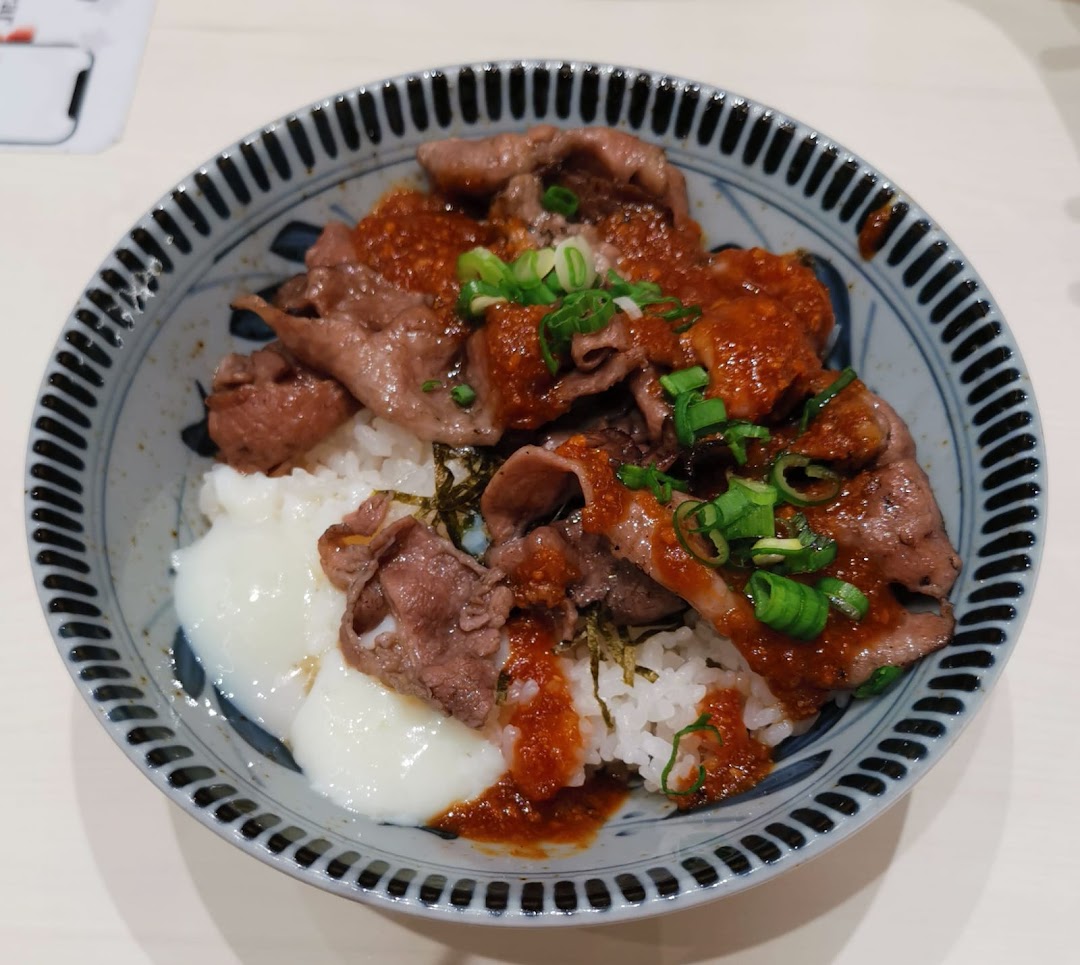 A close-up of a delicious Japanese beef bowl with rice, tender beef slices, spicy sauce, and a poached egg.